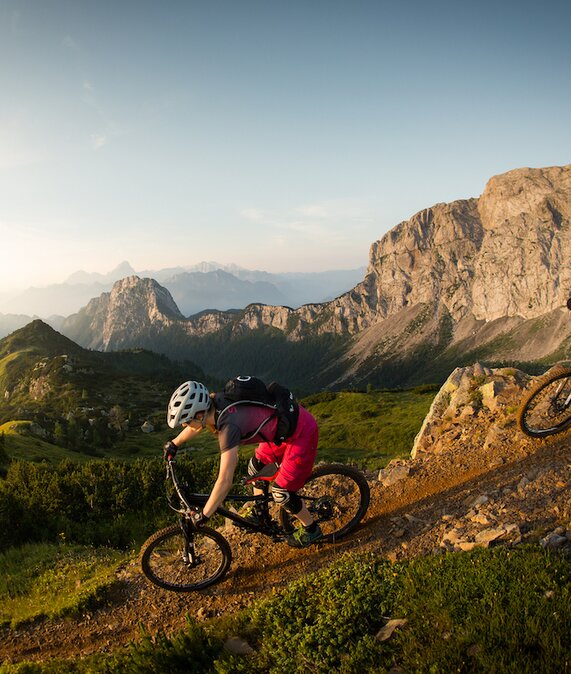 Mountainbiker fahren steilen Hang hinab mit herrlichem Bergpanorama