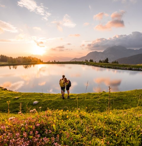 Wanderpaar am See bei Sonnenuntergang inmitten blühender Wiese