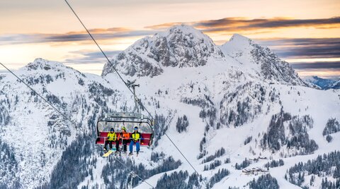 Skifahrer:innen am Sessellift bei Sonnenaufgang