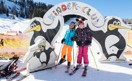 Zwei Kinder auf den Skiern vor einem Tor zum Kinderclub